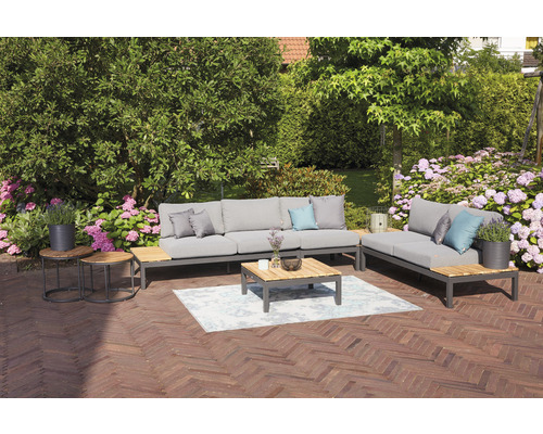 Ensemble de meubles de jardin avec canapé, chaise longue, table basse et tables d''appoint sur une terrasse avec des fleurs en arrière-plan.