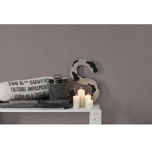 Scène décorative avec coussin, boîte, bougies et une grande sculpture de lettre devant un mur à motifs.