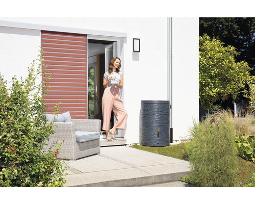 Récupérateur d''eau de pluie dans le jardin à côté d''une femme et d''une maison