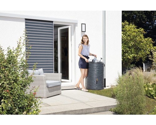 Une femme arrose des plantes avec de l''eau de pluie provenant d''un récupérateur d''eau de pluie dans le jardin.