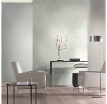 Salon lumineux avec papier peint à motifs floraux, fauteuils et lampadaire.