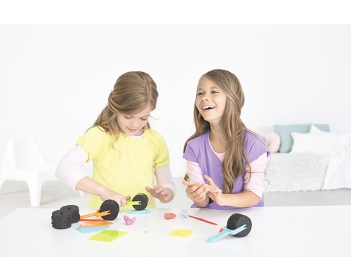 Zwei Mädchen sitzen an einem Tisch und spielen mit Knete und Werkzeugen.