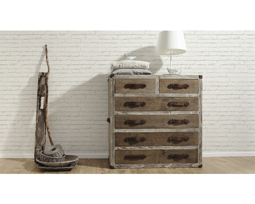 Kommode aus Holz mit sechs Schubladen, Dekoration und Lampe vor einer Ziegelwand