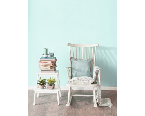 Szene mit Schaukelstuhl, Beistelltisch, Büchern und Dekorationsgegenständen in einem hellen Raum.