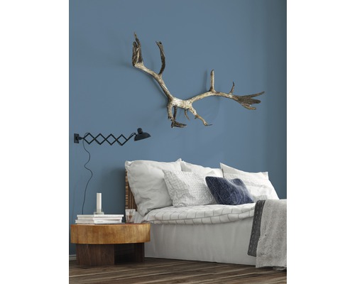 Schlafzimmer mit Bett, Nachttisch, Lampe und Geweih an der Wand.