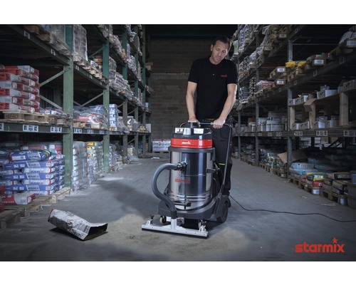 Ein Mann bedient einen Industriesauger in einem Lagerhaus mit Warenregalen.