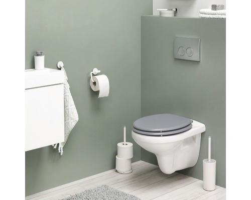 Salle de bains moderne avec WC suspendu, support papier toilette, brosse de toilette et meuble sous-lavabo.