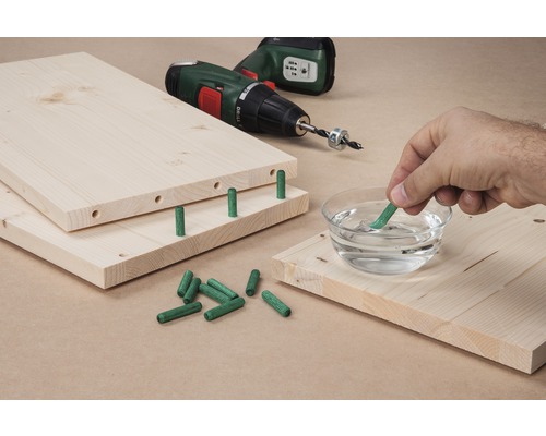 Planches en bois avec chevilles, perceuse et main trempant une cheville dans l''eau