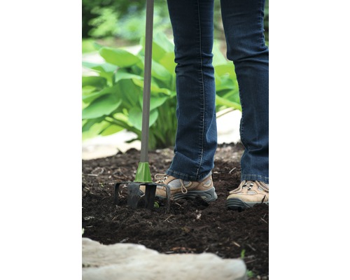 Une personne utilise un cultivateur dans le jardin pour ameublir le sol.