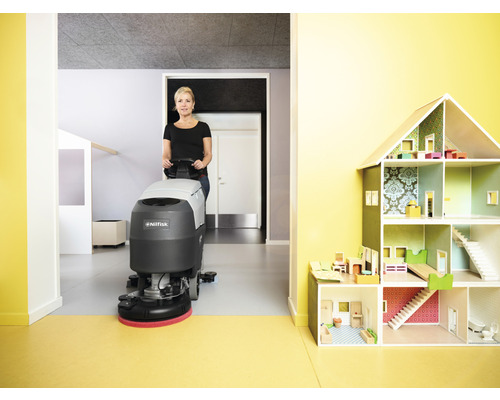 Femme utilisant une autolaveuse Nilfisk dans une pièce avec une maison de poupée.