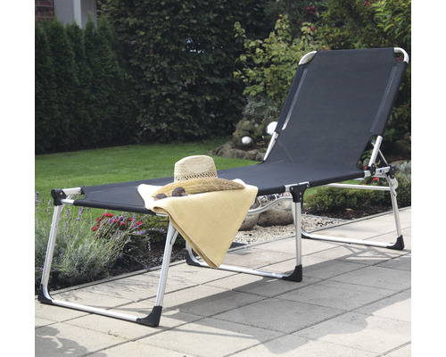 Gartenszene mit einer schwarzen Sonnenliege mit verstellbarer Rückenlehne, Handtuch, Hut und Sonnenbrille