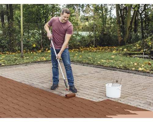 Ein Mann streicht Pflastersteine mit einer Farbrolle im Außenbereich.