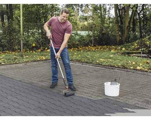 Mann streicht Pflastersteine mit Farbroller im Aussenbereich.