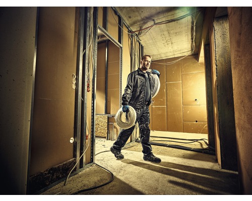 Artisan portant une bobine de câble dans une construction brute