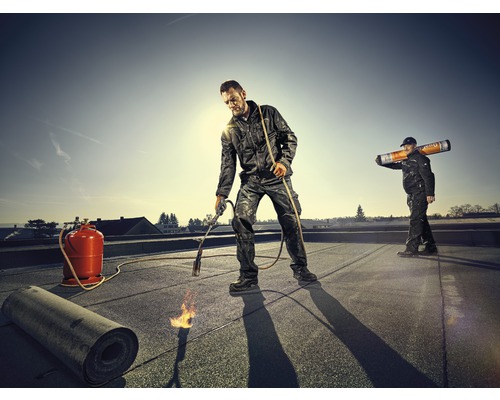 Couvreurs travaillant avec un chalumeau et une bouteille de gaz sur un toit.