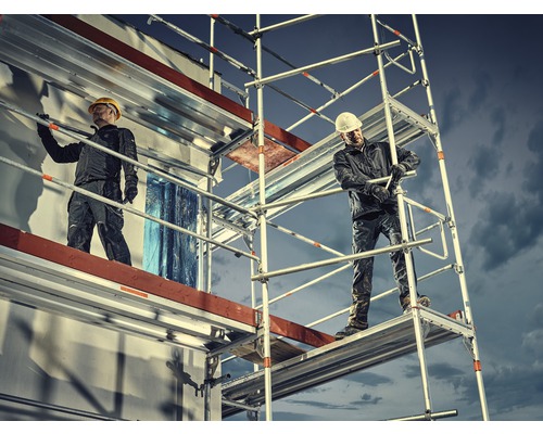 Deux artisans sur un échafaudage devant un bâtiment en travaux.