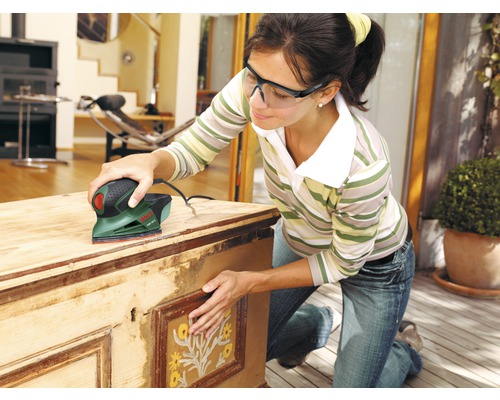 Frau schleift Holztruhe mit einem Elektroschleifer