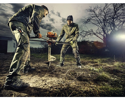 Deux ouvriers creusent un trou dans le sol à l''aide d''une tarière thermique.