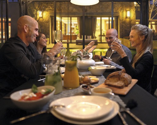 Un groupe de personnes est assis à une table dressée et apprécie un repas dans une atmosphère lumineuse et accueillante.