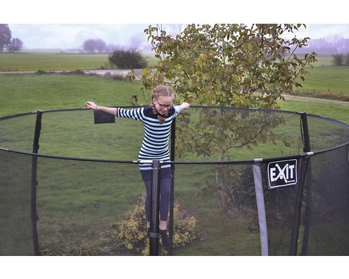 Fille en équilibre sur un trampoline de jardin avec filet de sécurité. Logo EXIT.