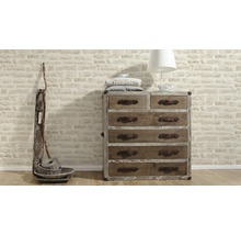 Commode à tiroirs avec lampe, coussins et décoration devant un mur de pierre