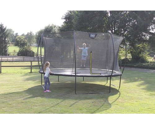 Trampoline avec filet de sécurité dans le jardin avec des enfants qui jouent
