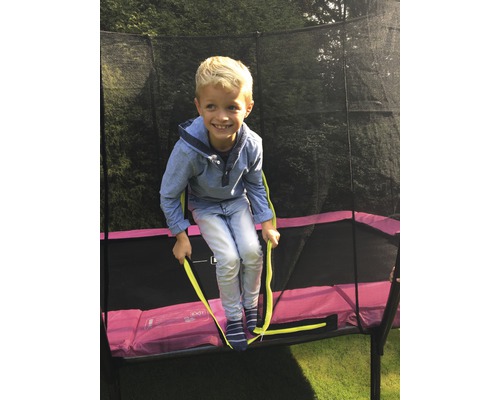Un enfant grimpe sur un trampoline de jardin avec filet de sécurité.
