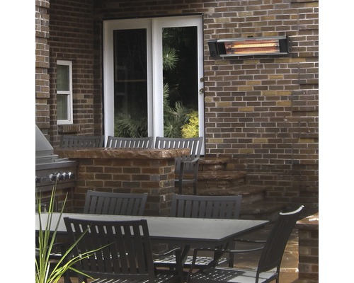 Terrassenszene mit Infrarot-Heizstrahler an Ziegelwand über Gartentisch und Stühlen.