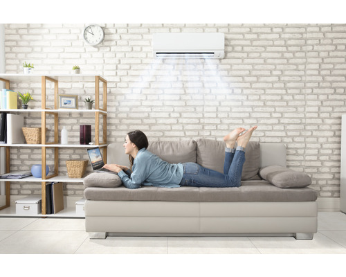 Femme allongée sur un canapé sous un climatiseur avec un ordinateur portable