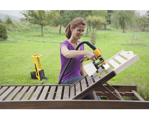 Une femme utilise un système de pulvérisation de peinture pour peindre un transat en bois dans le jardin.