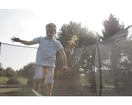 Un enfant saute sur un trampoline de jardin avec filet de sécurité.