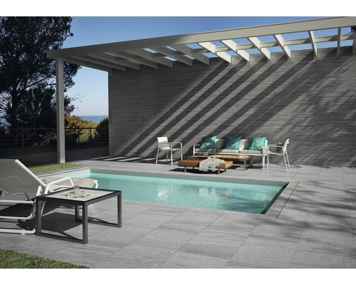 Terrasse avec piscine, sol carrelé, revêtement mural et coin salon sous une pergola.