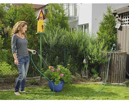 Frau giesst Blumen mit einem Gartenschlauch im Garten.