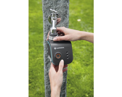 Eine Person befestigt einen Gardena Smart Water Control Bewässerungscomputer an einem Wasserhahn im Freien.