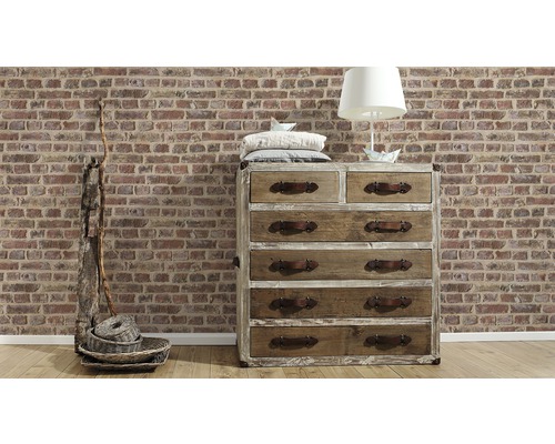 Commode en bois avec tiroirs, lampe et décoration devant un mur en briques