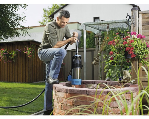 Mann bedient eine Tiefbrunnenpumpe an einem Brunnen im Garten.