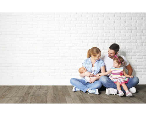 Une famille est assise sur un plancher en bois devant un mur de briques.