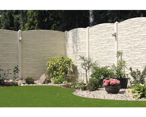 Scène de jardin avec une clôture en aspect pierre, des plantes et une pelouse