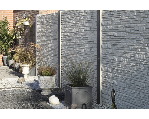 Scène de jardin avec clôture en béton et pots de fleurs plantés.