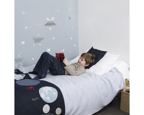 Garçon lit un livre dans une chambre d''enfant avec des stickers muraux étoiles et du linge de lit avec des motifs de planètes
