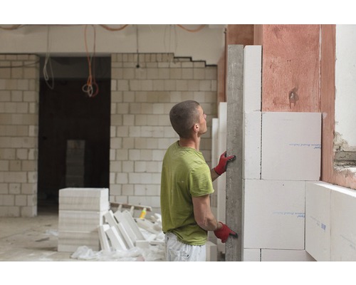 Un homme construit un mur en béton cellulaire dans une pièce inachevée.