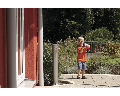 Junge mit Wasserpistole neben einem Gartenwasserhahn