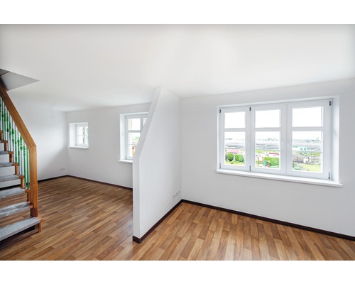 Pièce lumineuse avec parquet, escalier et fenêtres blanches.