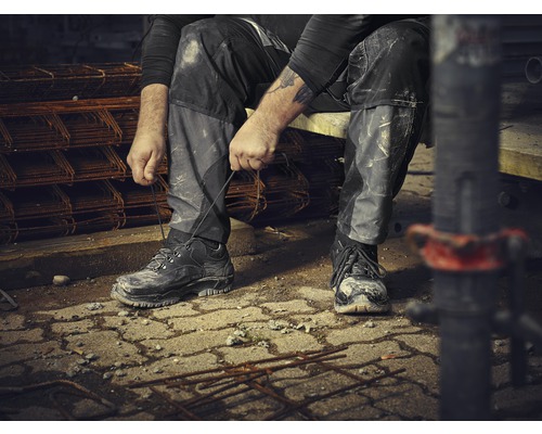 Un ouvrier du bâtiment est assis et noue ses chaussures de travail sur un chantier.
