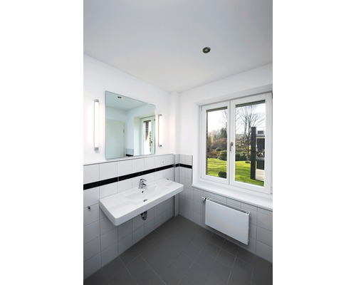 Badezimmer mit Waschbecken, Spiegel, Heizkörper und Fenster mit Blick ins Grüne