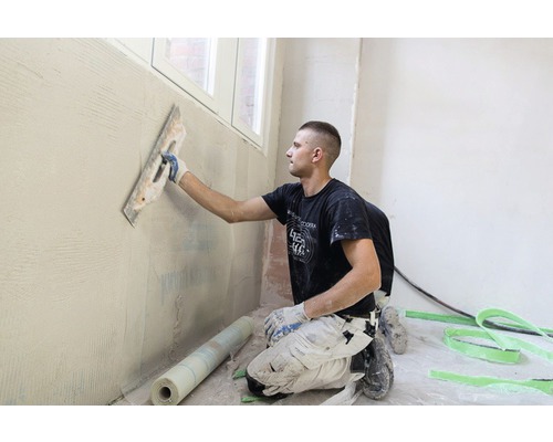 Un artisan applique du plâtre sur un mur avec une taloche.