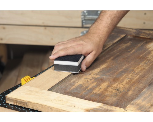 Eine Person schleift eine Holzoberfläche mit einem Schleifklotz