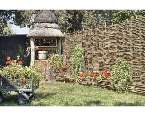 Scène avec puits de jardin, clôture en osier, chariot à fleurs et bacs à fleurs en osier