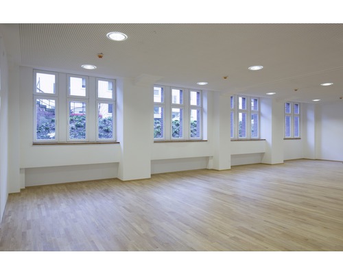 Heller Raum mit Holzboden, weißen Wänden und großen Fenstern