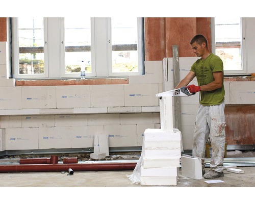 Ein Mann sägt Porenbetonsteine mit einer Porenbetonsäge in einem Rohbau.